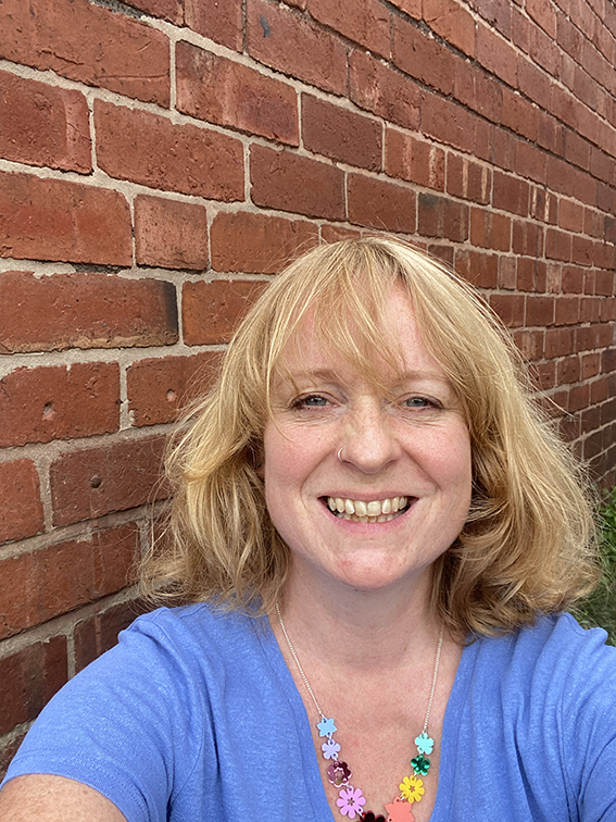 The founder of Black Bee Creative, Steph, stood in front of a brick wall, smiling at the camera.